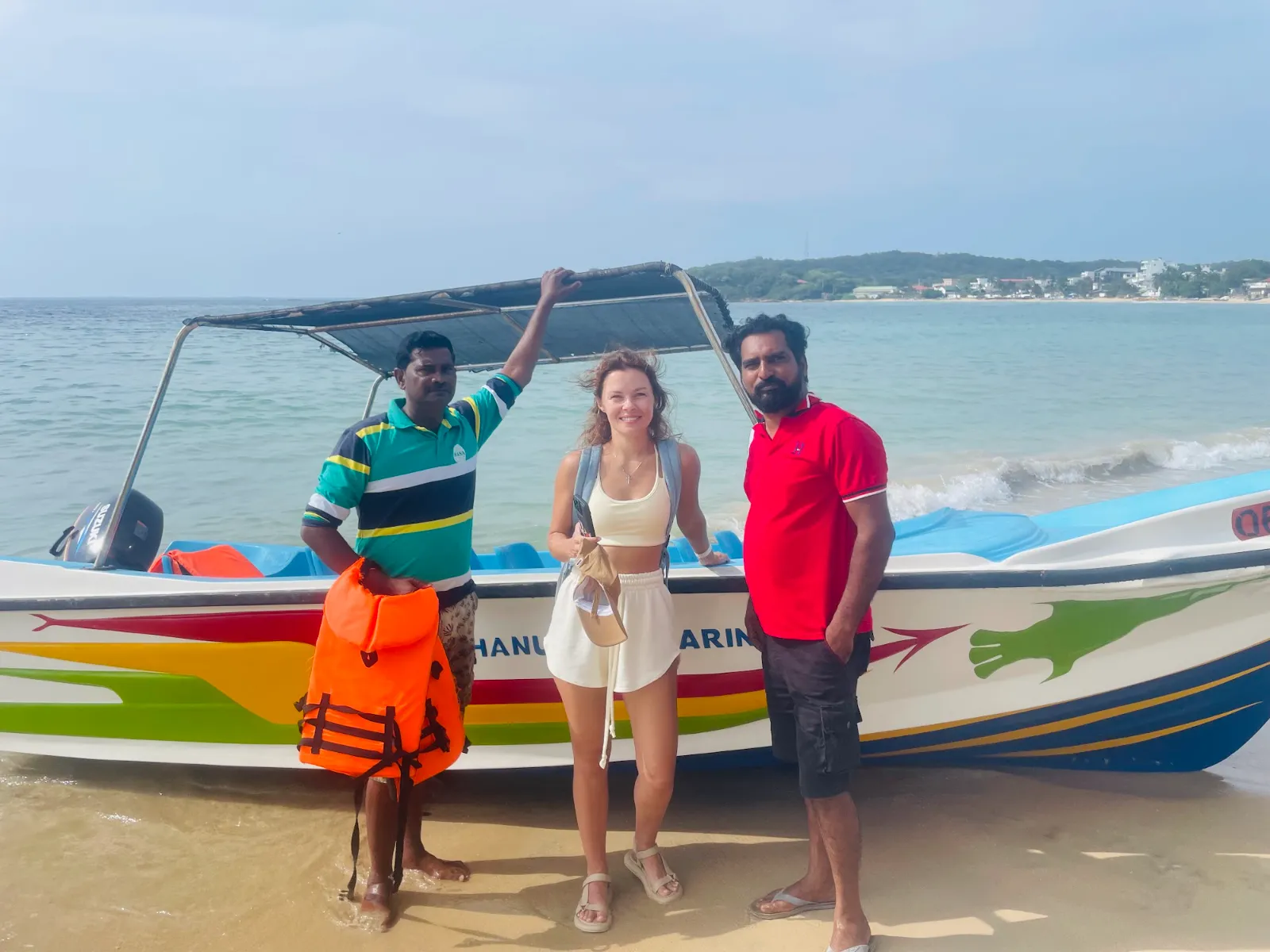 Guests standing beside a painted fishing boat on the beach in Trincomalee