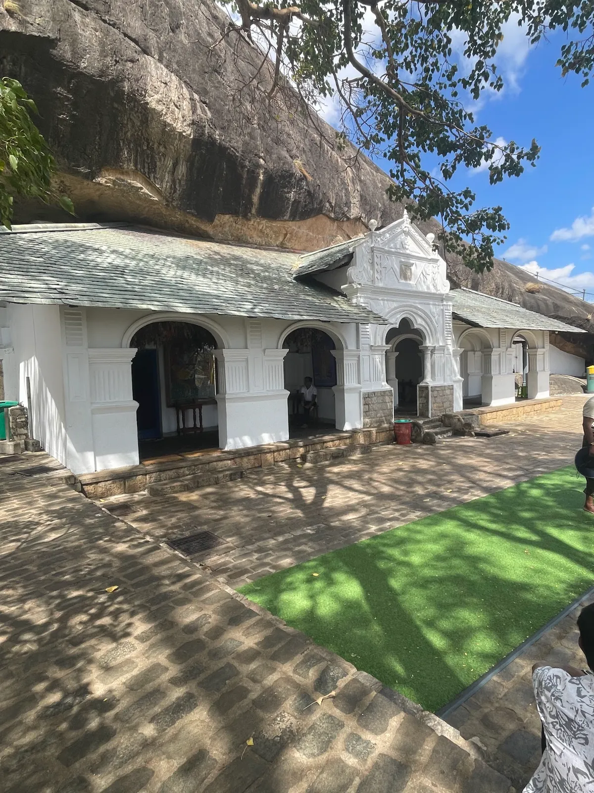 White entrance buildings of the Dambulla cave temple beneath a huge overhanging rock